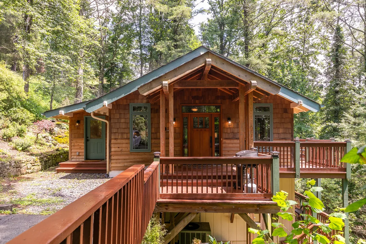 This image captures the inviting front porch of the property, featuring wooden railings, natural wood siding, and landscaped greenery surrounding the entrance. The porch overlooks the wooded environment, suggesting a seamless transition from indoor comfort to outdoor adventure.