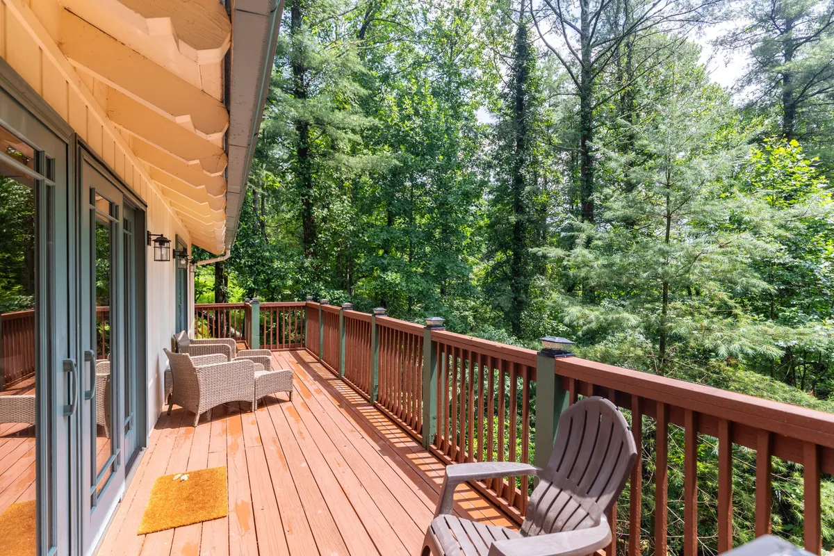 A peaceful wooden deck set amidst dense trees, featuring outdoor seating for enjoying nature’s sights and sounds. The deck appears private and nestled away from the main house, emphasizing seclusion and the ability to stargaze or watch wildlife.