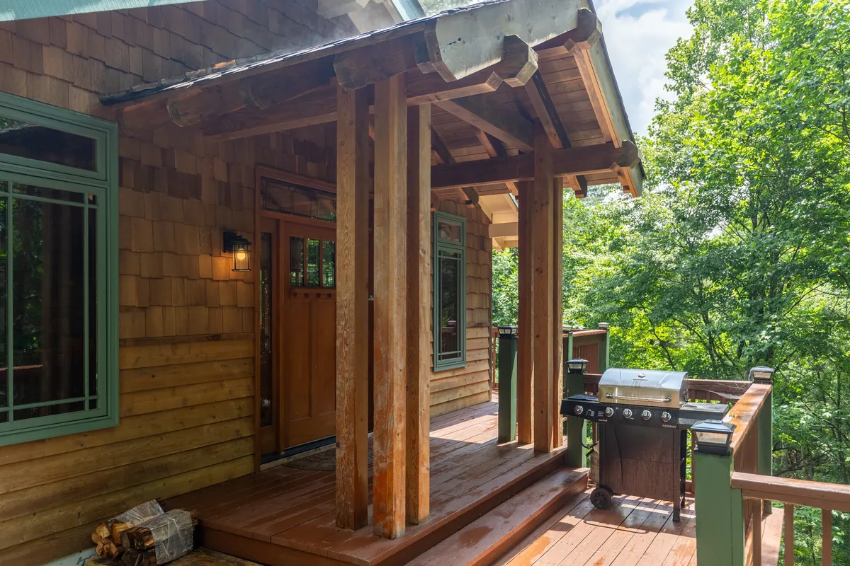 This image offers a view of the front door and porch area, accented by sturdy wooden columns, a grill, and a classic porch railing. The porch space is designed for gathering, relaxing, and provides easy access to outdoor spaces.