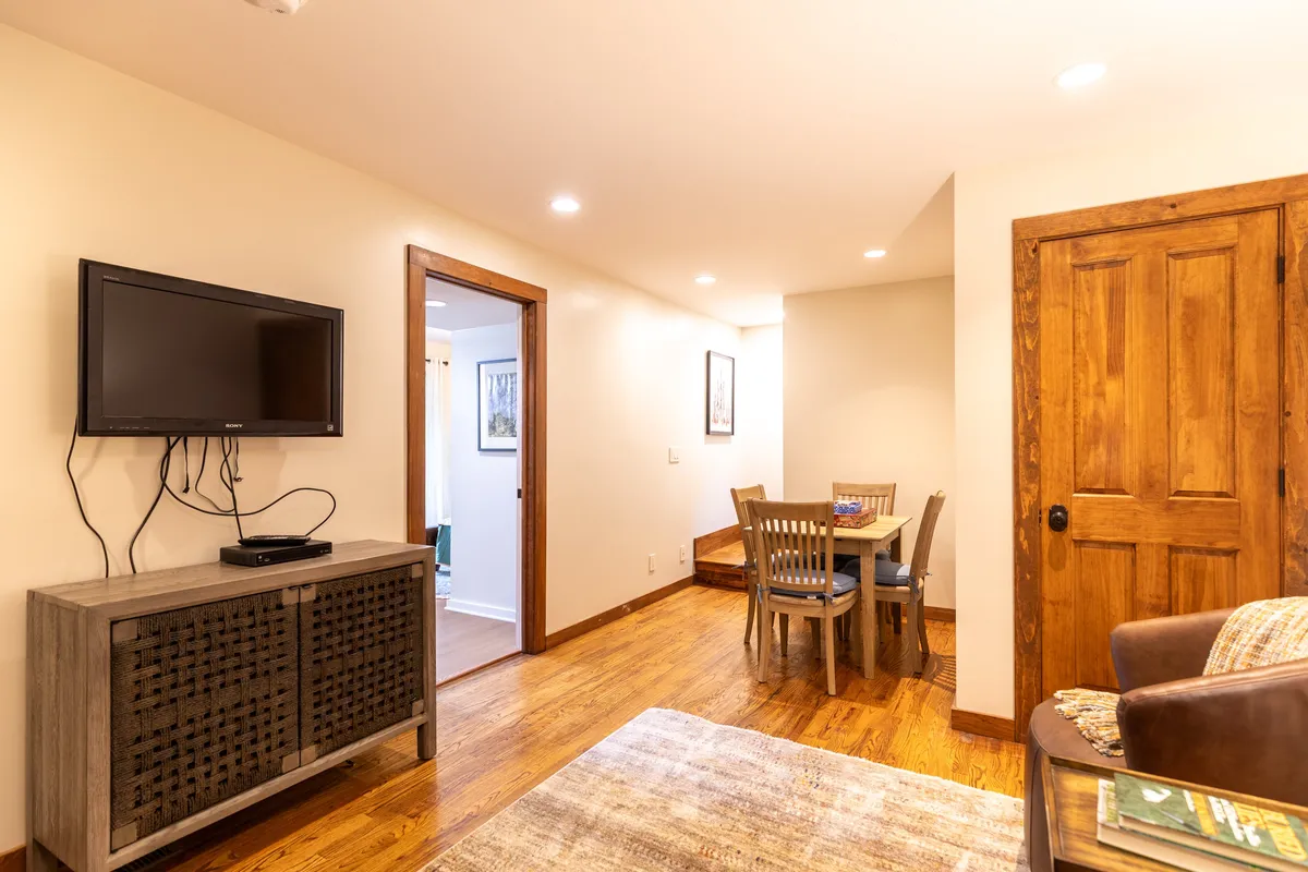 A warm, welcoming dining space showcases a sturdy dining table set for a family meal, with a television and decorative rug in the background. The mood is cozy, suggesting the enjoyment of shared meals and relaxed moments together.