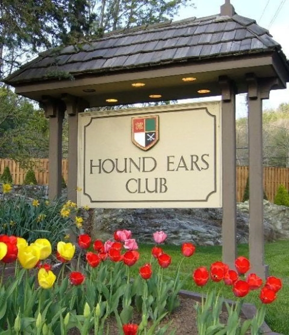 This exterior image showcases the welcoming signage of the Hound Ears Club surrounded by a colorful, manicured flower bed. The setting is inviting and hints at a friendly community atmosphere, with plenty of open space for outdoor activities and gatherings.