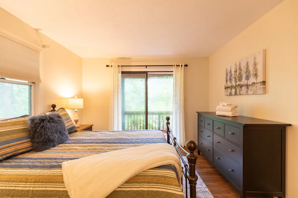 A cozy bedroom highlighted by a neatly made bed, window view, dresser, and tasteful artwork. The abundance of natural light creates a calm and restful environment ideal for unwinding after a day of exploration.