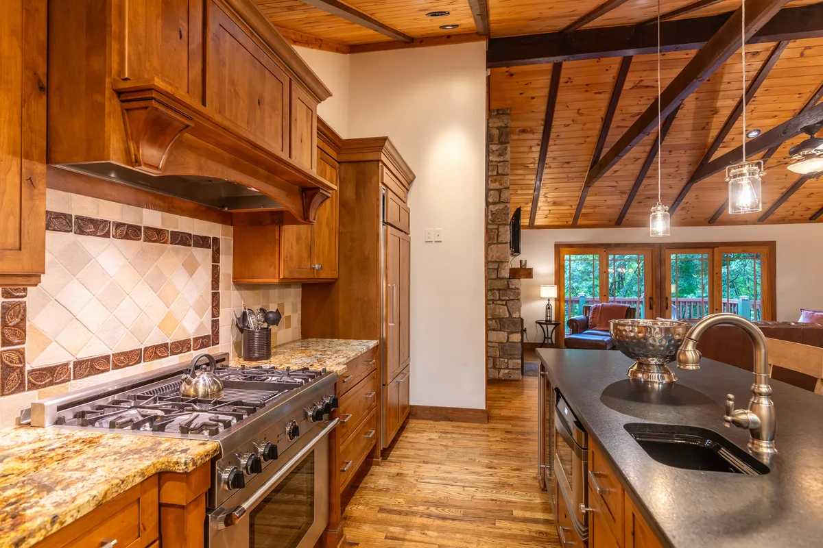 A kitchen with granite countertops, wooden cabinetry, a large window with a scenic view, and a prominent stone chimney. The design is both functional and inviting, suggesting opportunities for home-cooked meals and warm gatherings.