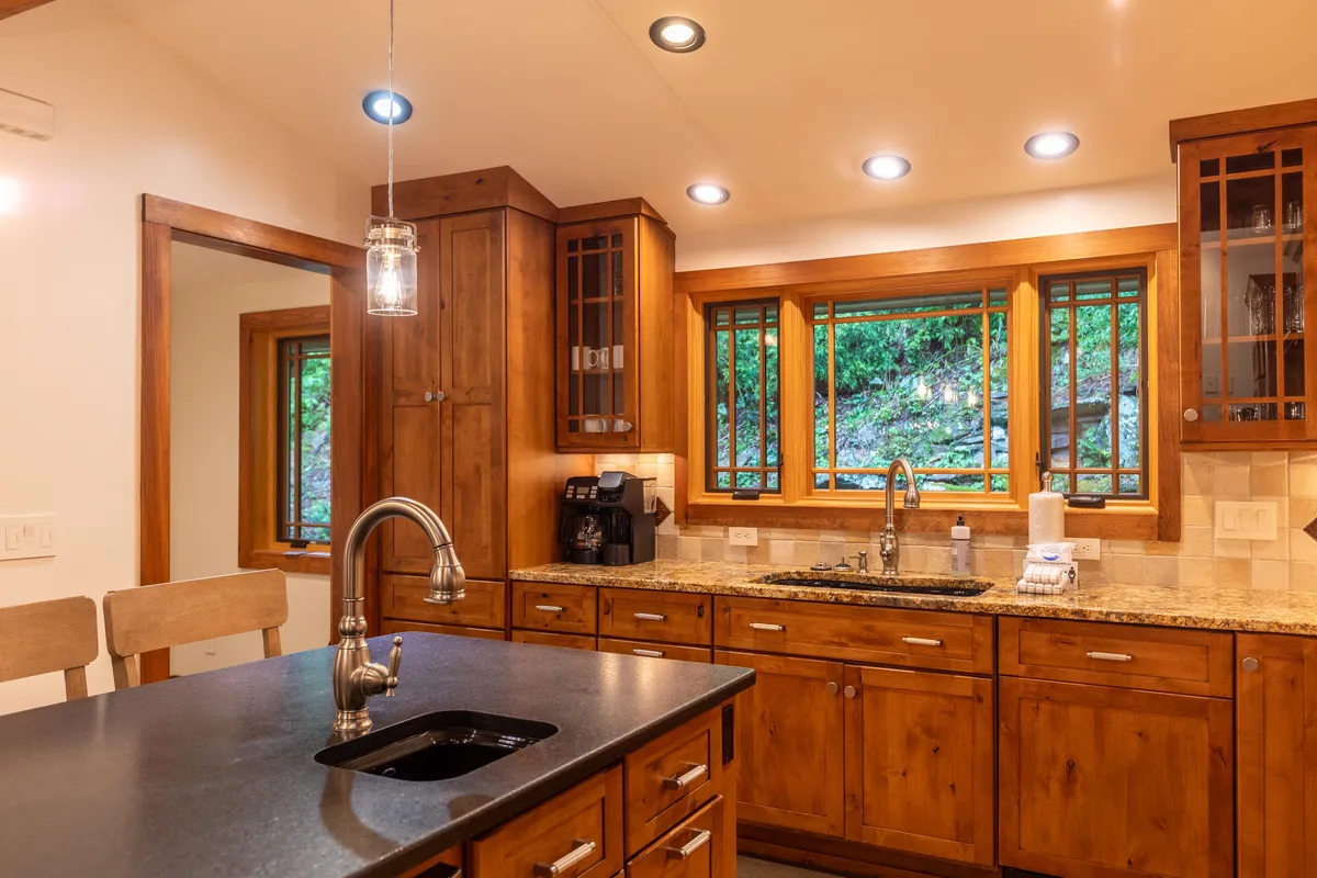 This image centers on a luxury kitchen with a prominent kitchen island, gleaming granite countertops, rich wood cabinetry, and a window framing a scenic view. The scene captures meal preparation, hinting at friendly gatherings and shared cooking experiences.
